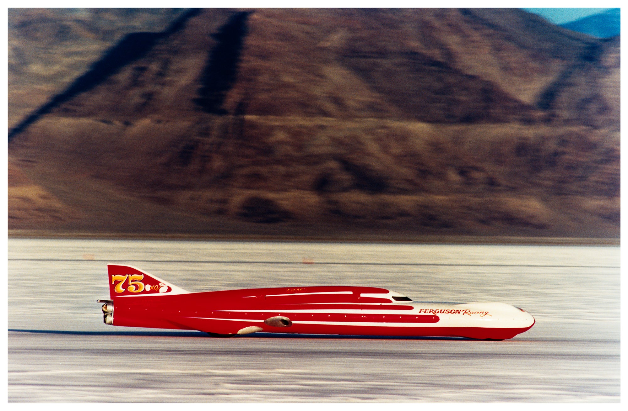Photograph by Richard Heeps.  A Red Ferguson Racing Streamliner sits on a smooth salt flat with mountains in the background.