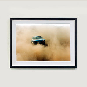 Black framed photograph by Richard Heeps.  A light blue Buick car moving towards the camera and slightly obscured by the dust clouds which it has created.