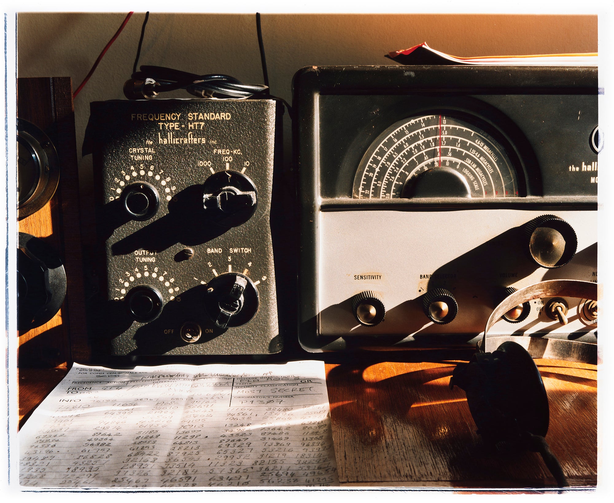 Photograph by Richard Heeps. Station X sits on a desk in front of it is a handwritten sheet of numbers and headphones sit to the right hand side of the paper.