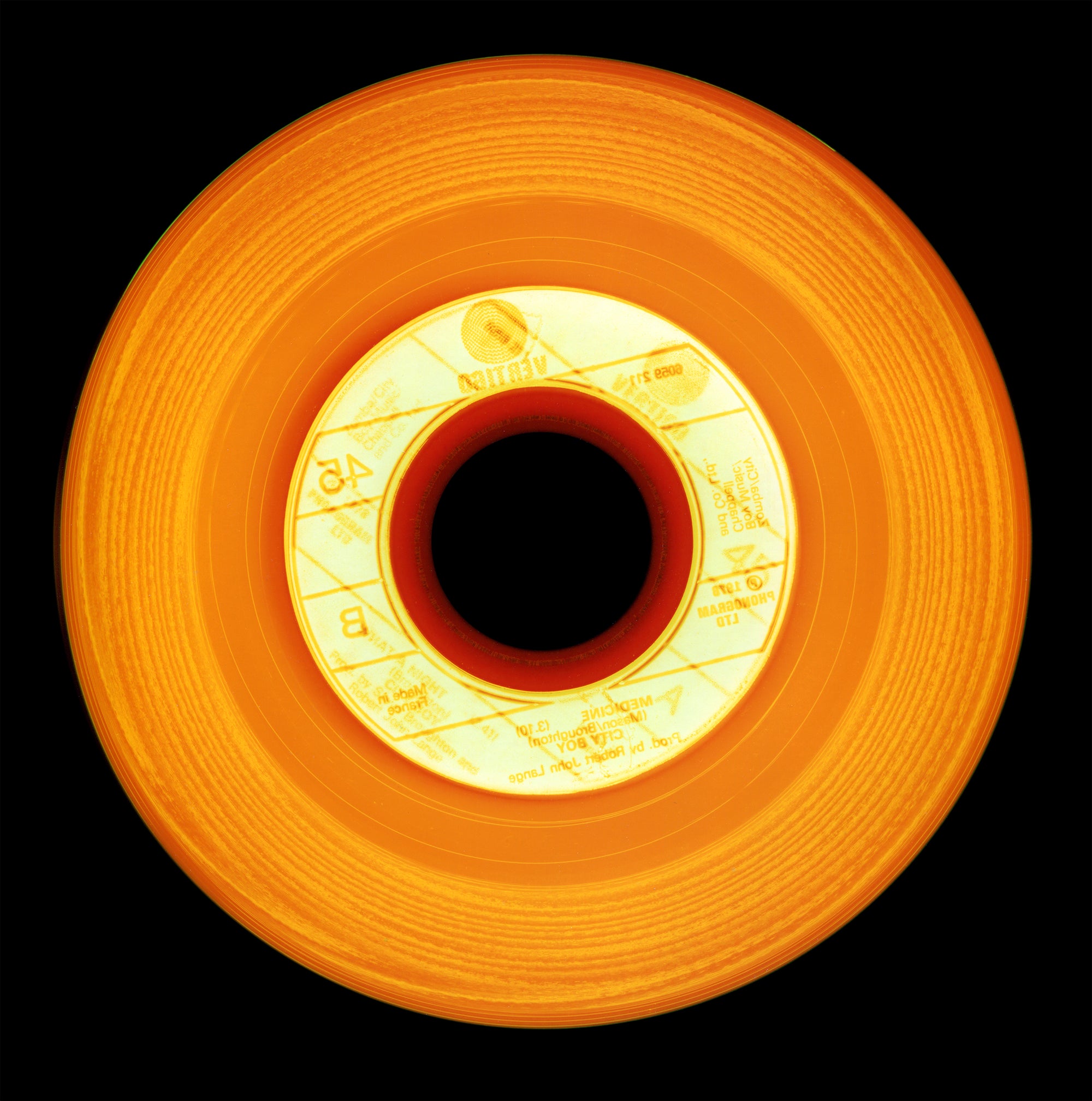 Photograph by Natasha Heidler and Richard Heeps.  An orange vinyl with a light orange record label.  Different tones of orange and red sit in the circular grooves of this record.  This sits on a black background.
