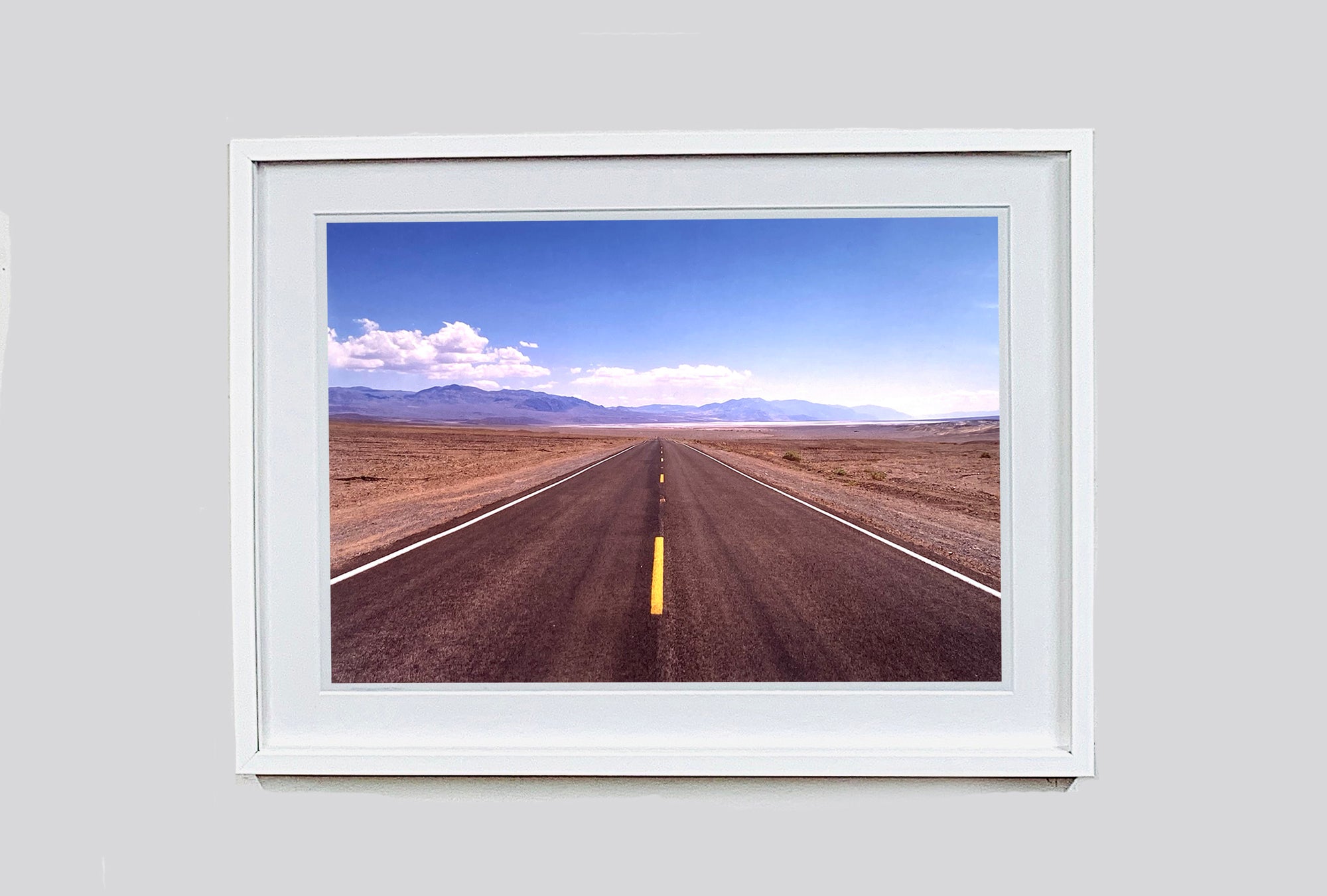 'The Road to Death Valley', taken in the Majova Desert, California, features a clouded blue sky met my mountains on the horizon. This American landscape artwork is part of Richard Heeps' 'Dream in Colour' series.