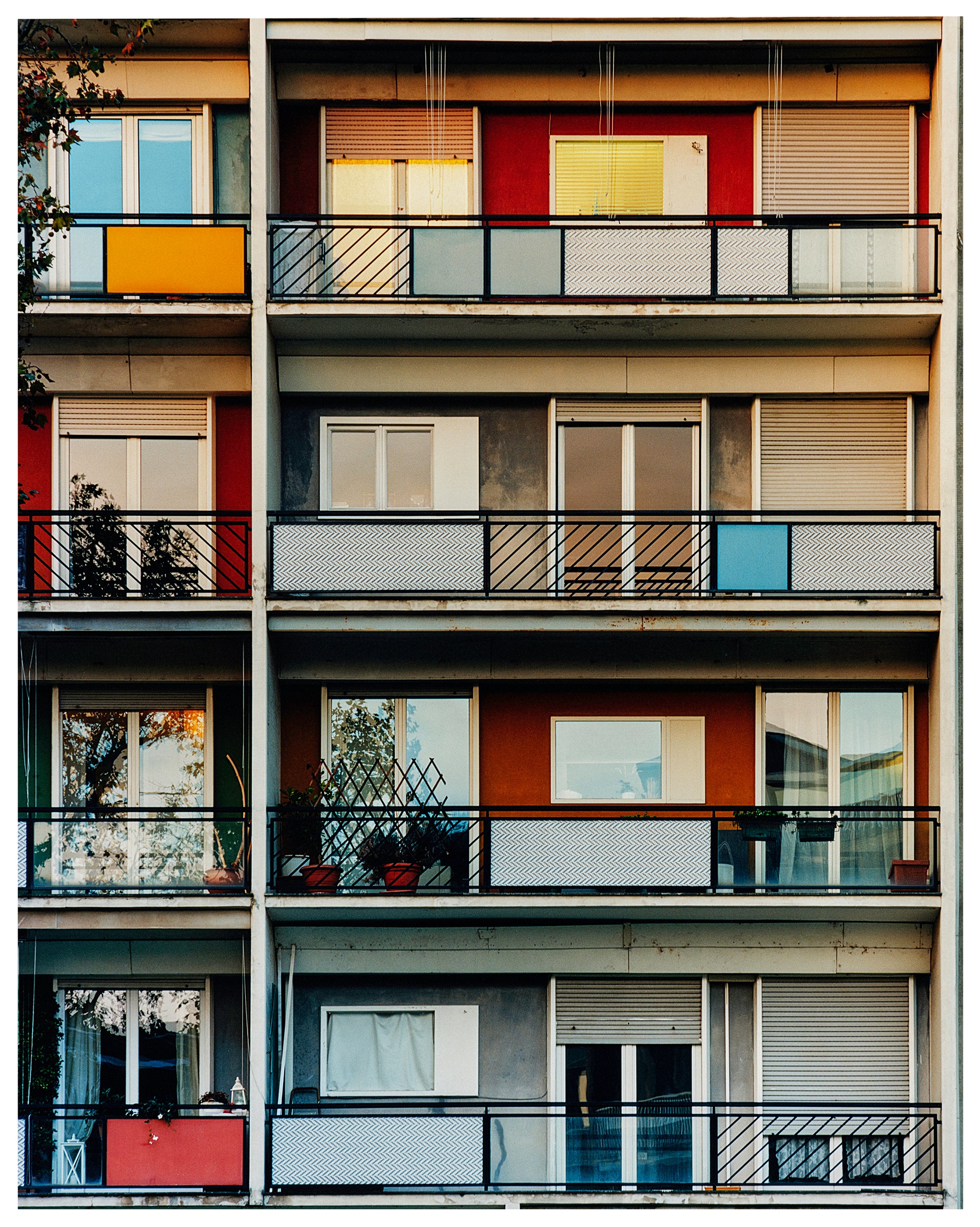 Photograph by Richard Heeps. This is the balconies and balcony doors of 4 floors of flats located on the Rue Dezza. The colours of the walls alternate between red and grey but look different as the light catches them.