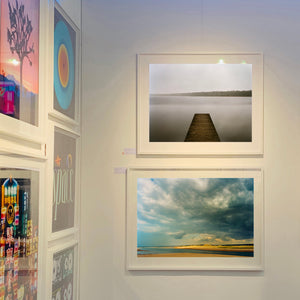 Framed artwork on a wall, including a dock scene and a landscape with clouds Norfolk photographic artworks by Richard Heeps.