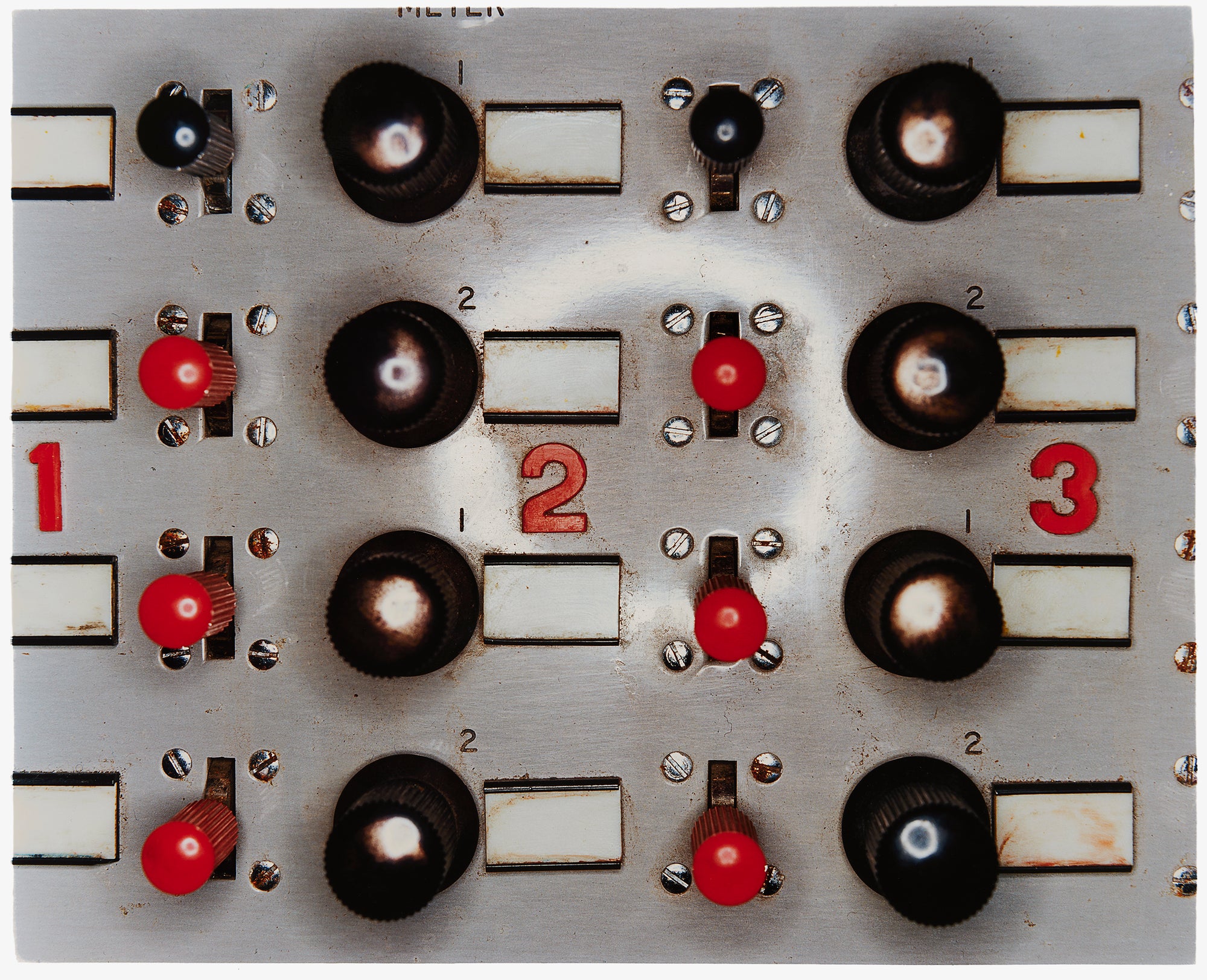 Photograph by Richard Heeps. A grey panel with four vertical lines of knobs alternating from left to right with three red knobs and one black knob, next to four black bigger knobs, this repeats. Then along the horizontal middle are numbers in red 1, 2 and 3.