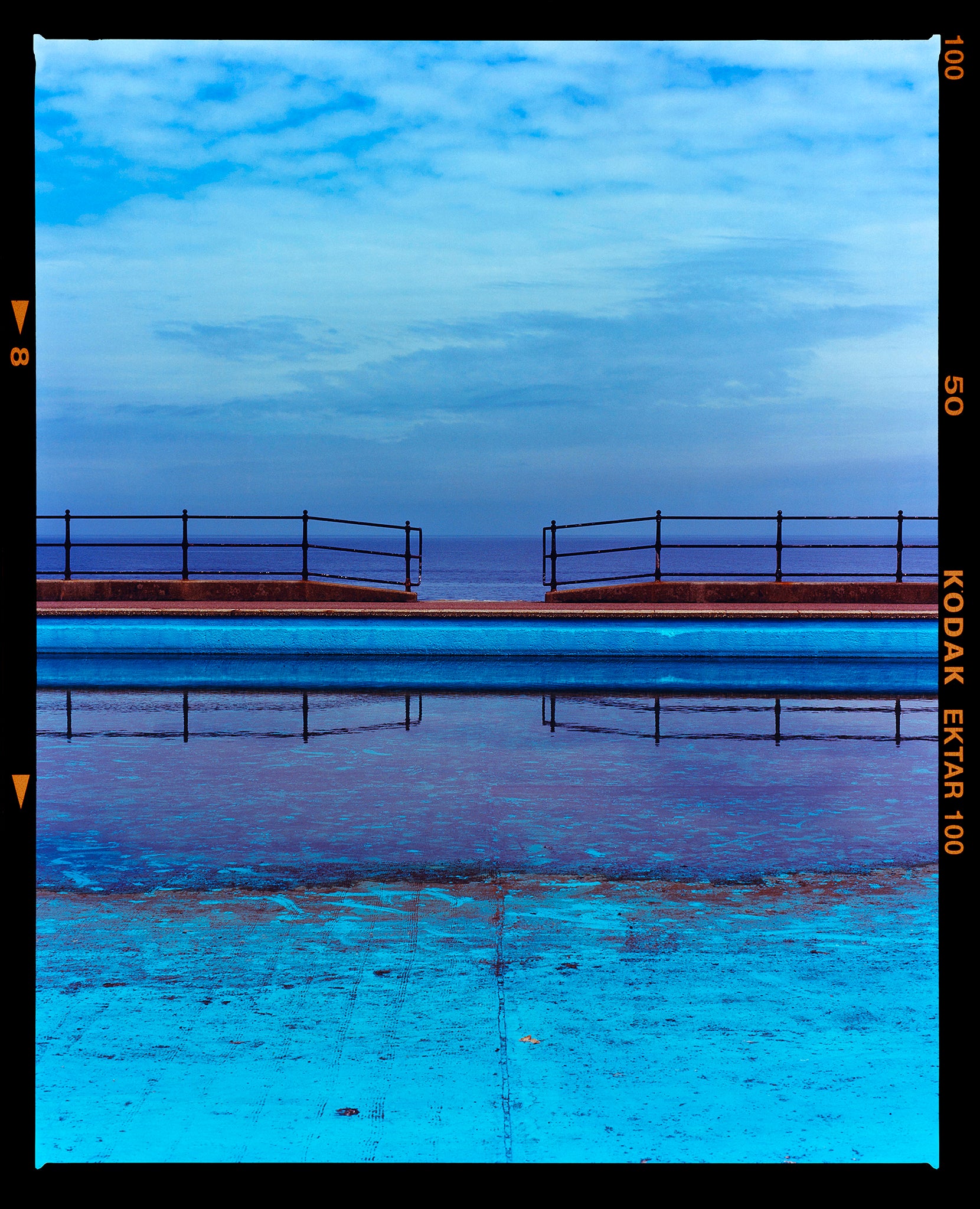 Photograph by Richard Heeps. The blue bay at Llandudno, cut across the middle with path and railings with a gap right in the middle.