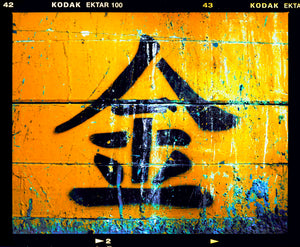 Photograph by Richard Heeps. A photograph of a worn sign featuring a Chinese symbol painted onto a gold back ground.