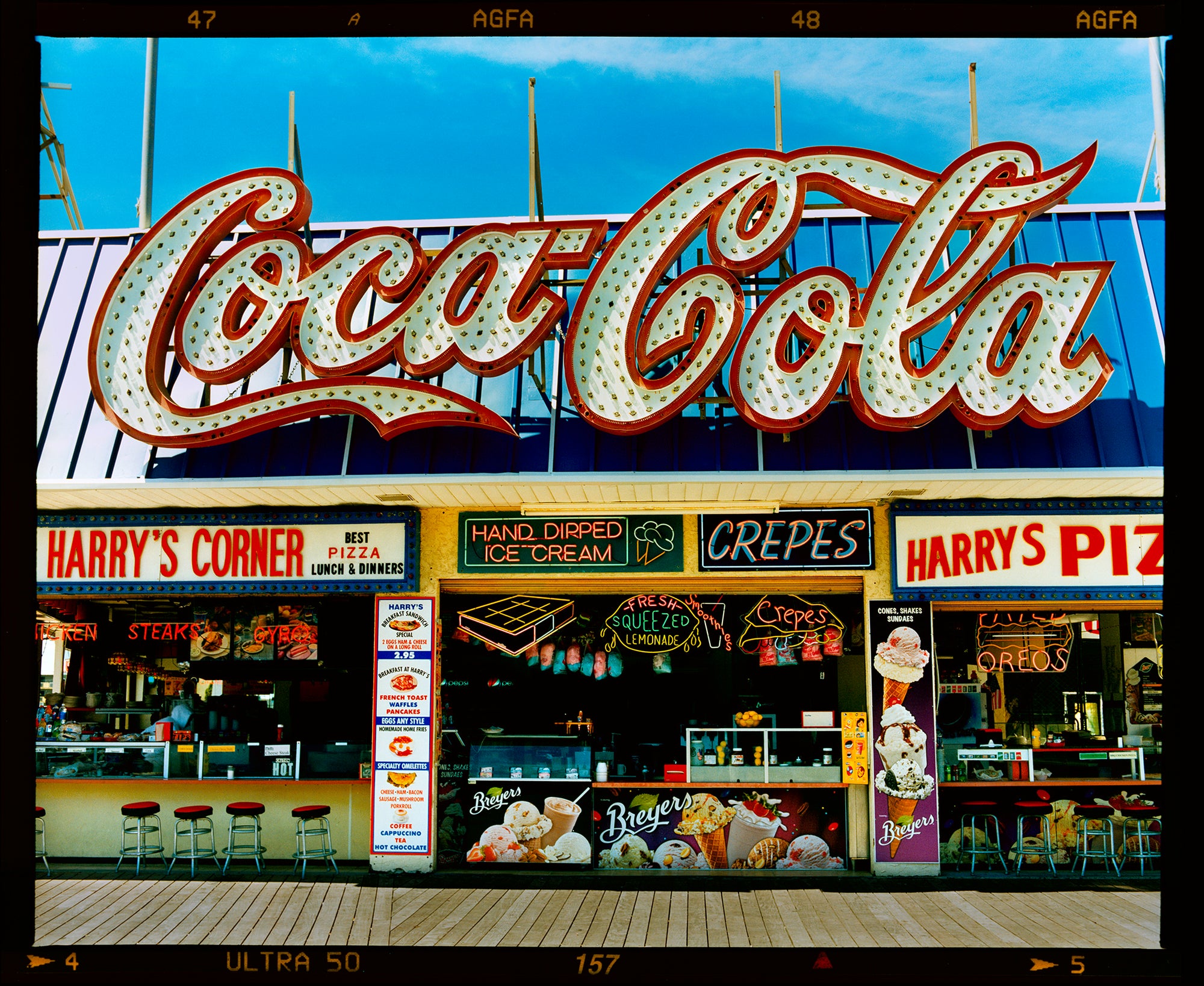 Photograph by Richard Heeps. Harry's Corner was taken on the wildwood boardwalk, featuring neon typography and the iconic Coca-Cola sign against a bright blue sky. 