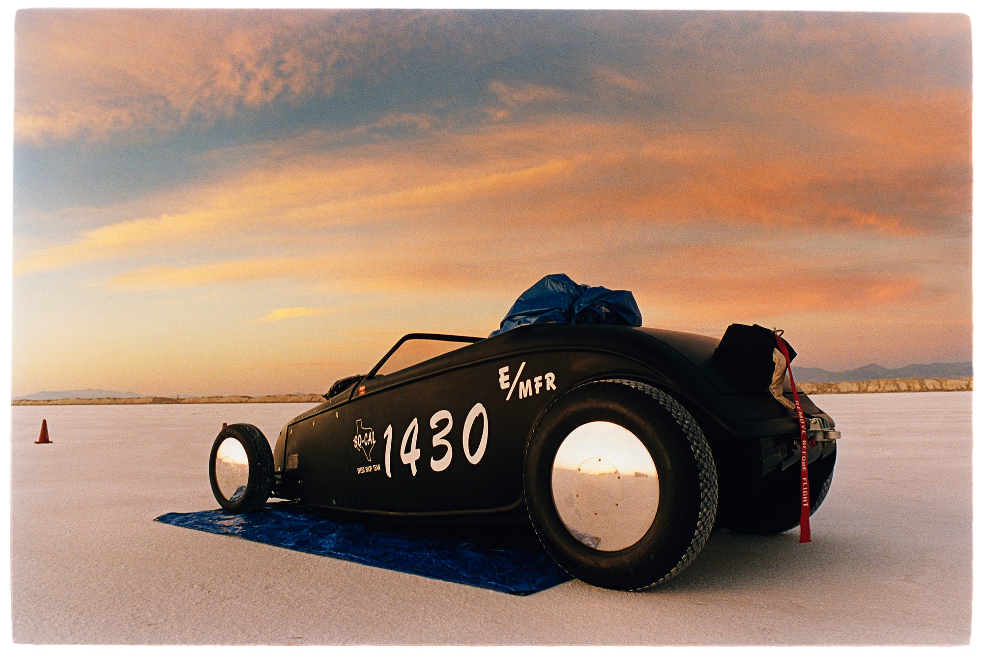 Photograph by Richard Heeps.  A roadstar sits on a smooth salt flat with mountains in the background.
