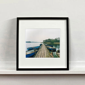 Ormesby Little Broad, a docking jetty with small boats stretches out to the Norfolk Broad photograph by Richard Heeps mounted square framed in black.