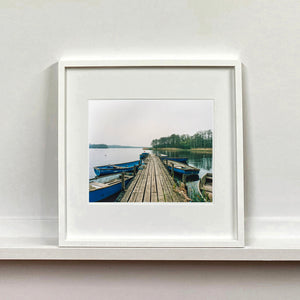 Ormesby Little Broad, a docking jetty with small boats stretches out to the Norfolk Broad photograph by Richard Heeps mounted square framed in white.