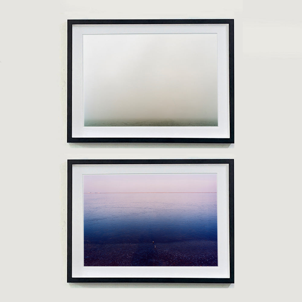 Two Black framed photographs by Richard Heeps. The top photograph is of a wonderfully thick fog and all you can make out is the dark grey of the fenland. The bottom photo shows a light sky at the top shading into a dark blue water at the bottom.