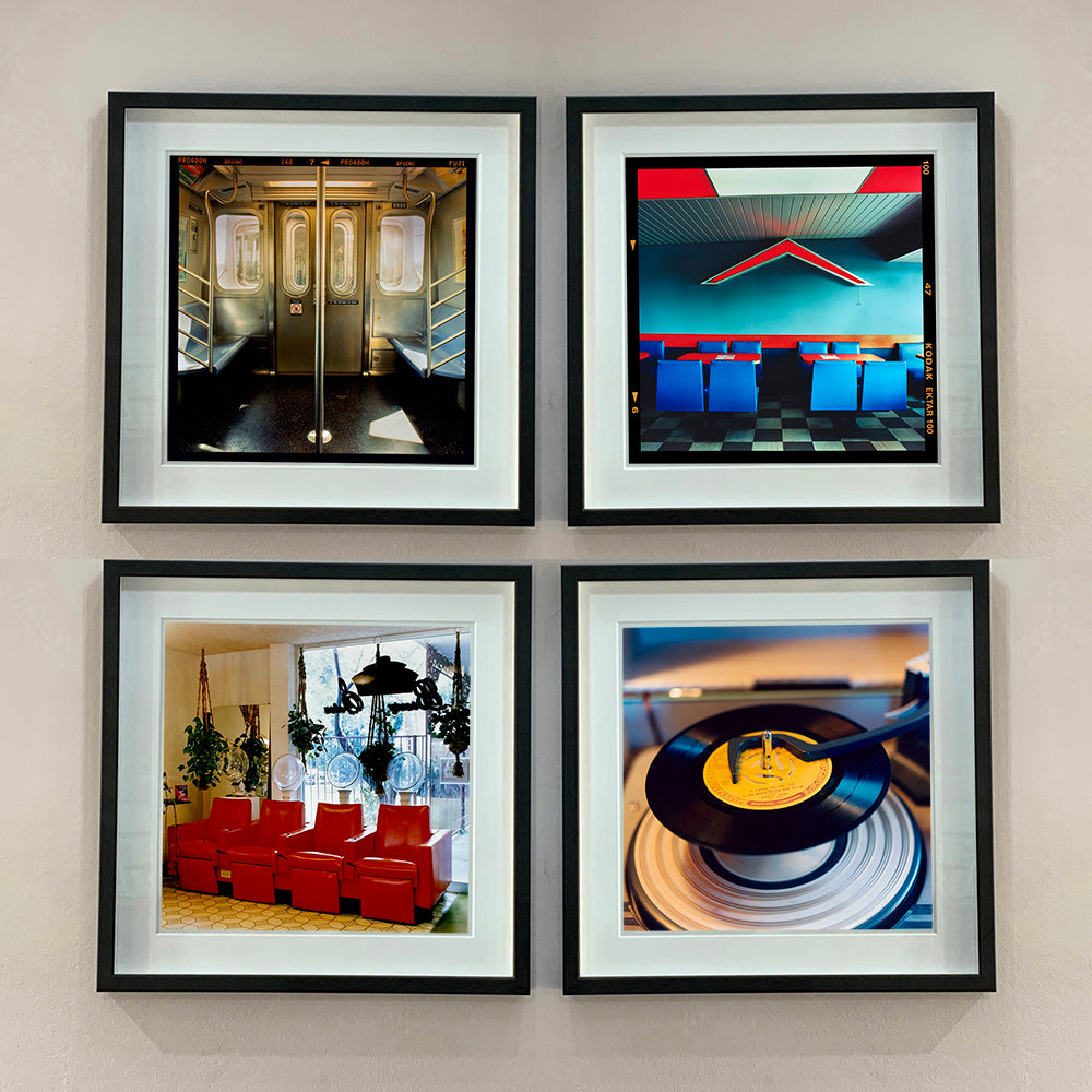 Four black framed photographs by Richard Heeps. Photographs of the inside of a subway car, the inside of a Wimpy in Norfoik. Bottom right is the photo of a vinyl record on a retro record player, bottom left is a photograph of 4 red retro chairs in a hair salon.