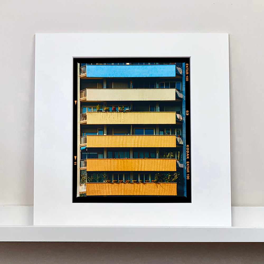 Photograph by Richard Heeps. Photograph of an apartment building with coloured balconies, blue at the top balcony and then fading from light yellow to a sunburnt yellow at the bottom.