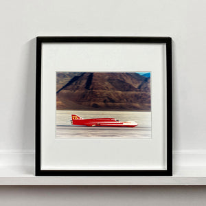 Black framed photograph by Richard Heeps.  A Red Ferguson Racing Streamliner sits on a smooth salt flat with mountains in the background.