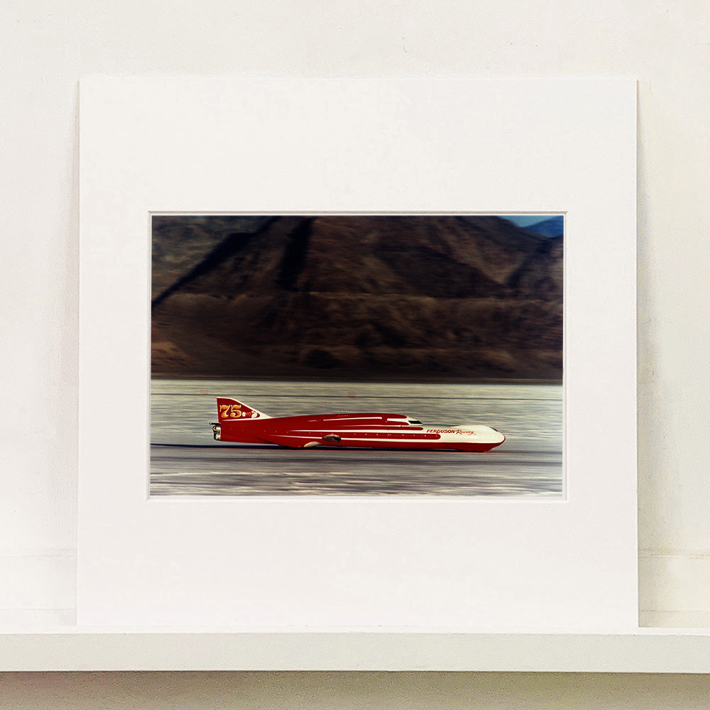 Mounted photograph by Richard Heeps.  A Red Ferguson Racing Streamliner sits on a smooth salt flat with mountains in the background.