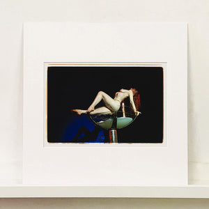 Mounted photograph by Richard Heeps. Burlesque Dancer arches her back while balancing over a human size champagne glass.