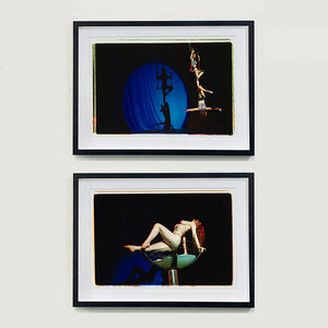 Two black framed photographs by Richard Heeps. The top photo is of two women on a trapeze, one sits on the swing and the other is hanging down from the first. The background is dark apart from a blue circle in which shows their acrobatic shadow. The bottom photo is a Burlesque dancer in a human size glass of champagne, she is arched backwards over the glass. 