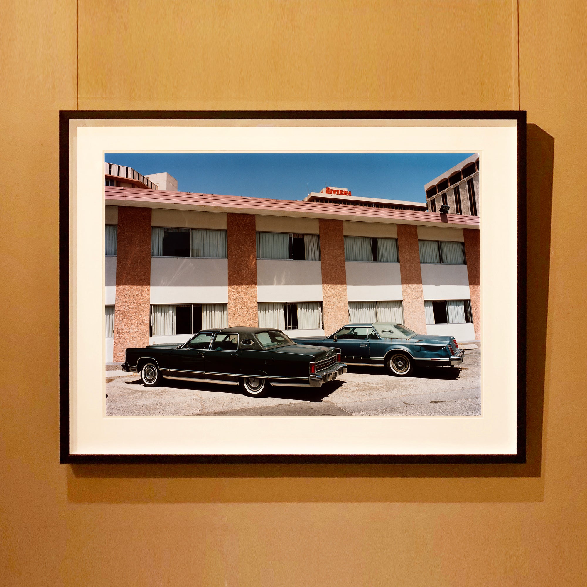Black framed photograph by Richard Heeps. Hanging on the wall, this retro photograph has two classic Lincoln cars parked outside a hotel in Las Vegas. 