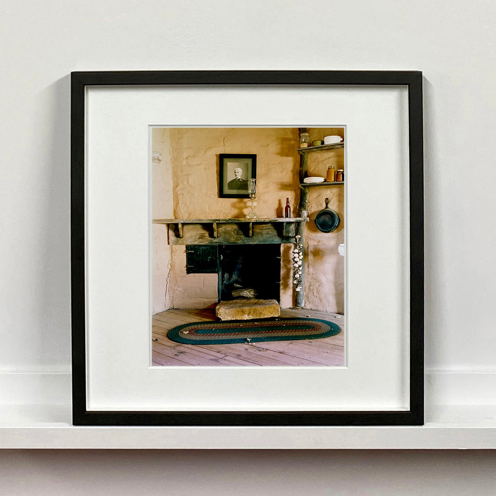 Black framed photograph by Richard Heeps. Film set of 'The Outlaw Josey Wales' featuring a wooden fireplace and a black and white photo over the mantlepiece.