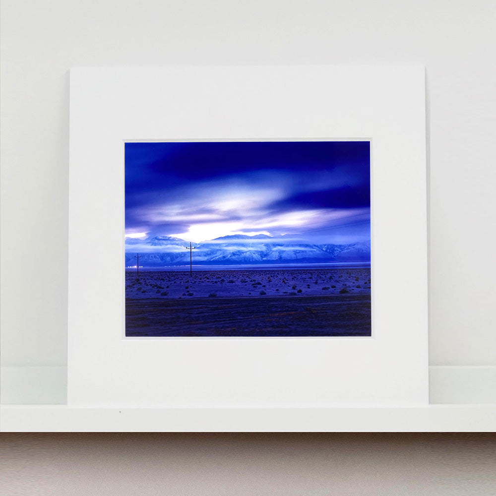 Mounted photograph by Richard Heeps. A blue light hits vast land, mountains and a big sky.