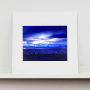 Mounted photograph by Richard Heeps. A blue light hits vast land, mountains and a big sky.