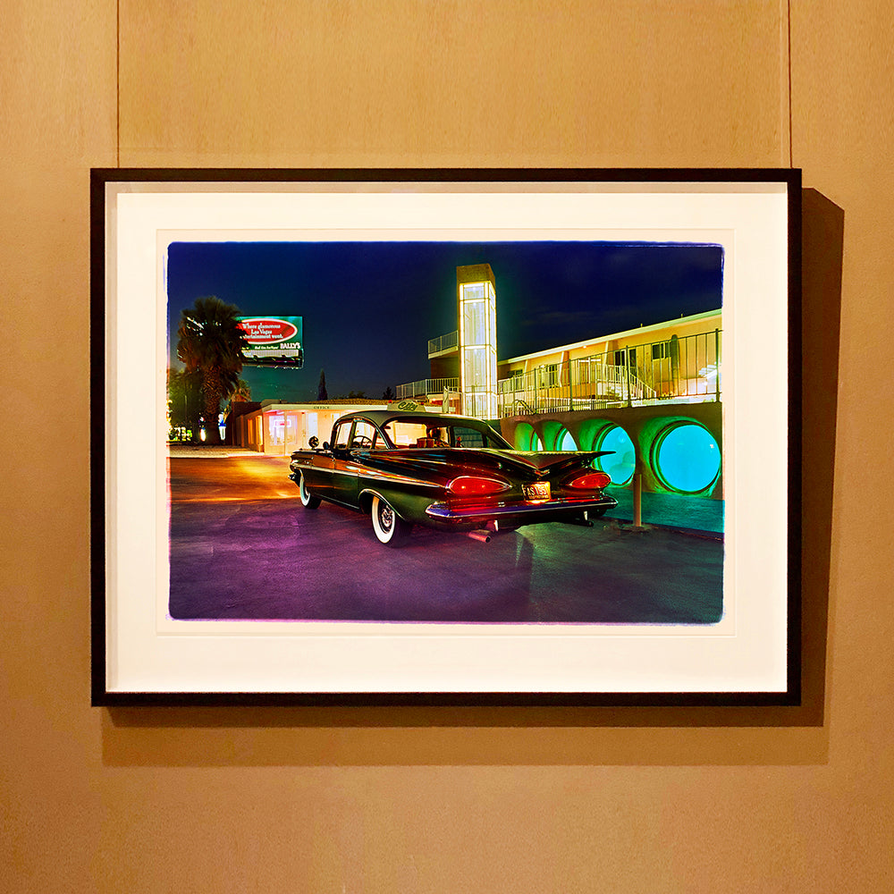 Black framed photograph by Richard Heeps. This photograph is hung on a wall and depicts a Chevy Bel Air central shot and off to the right are the pools and balcony of the Glass Pool Motel, Las Vegas.
