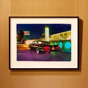 Black framed photograph by Richard Heeps. This photograph is hung on a wall and depicts a Chevy Bel Air central shot and off to the right are the pools and balcony of the Glass Pool Motel, Las Vegas.