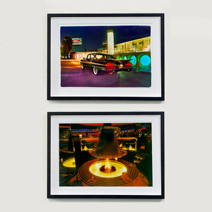 Two black framed photographs by Richard Heeps. Both retro photographs, one  has a Chevy Bel Air sitting in front of the Glass Pool Motel, Las Vegas. The photo at the bottom is an indoor fire pit surrounded by a circular table and a circular golden hood over the top.  The photo is taken in a mirrored bar which echoes the fire pit and hood all around this golden, dark lit bar.