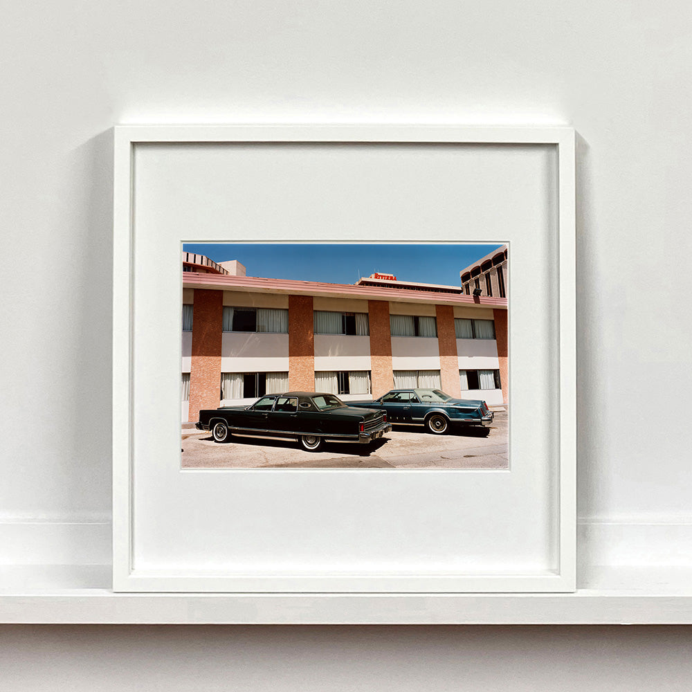 White framed photograph by Richard Heeps. This retro photograph has two classic Lincoln cars parked outside a hotel in Las Vegas. 