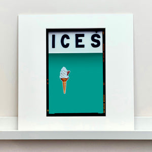 Mounted photograph by Richard Heeps.  At the top black letters spell out ICES and below is depicted a 99 icecream cone sitting left of centre against a Turquoise Teal coloured background.  