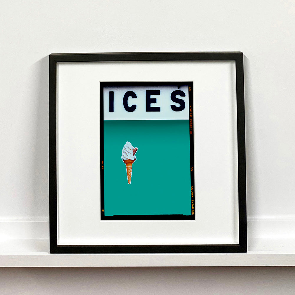 Black framed photograph by Richard Heeps.  At the top black letters spell out ICES and below is depicted a 99 icecream cone sitting left of centre against a Turquoise Teal coloured background.  