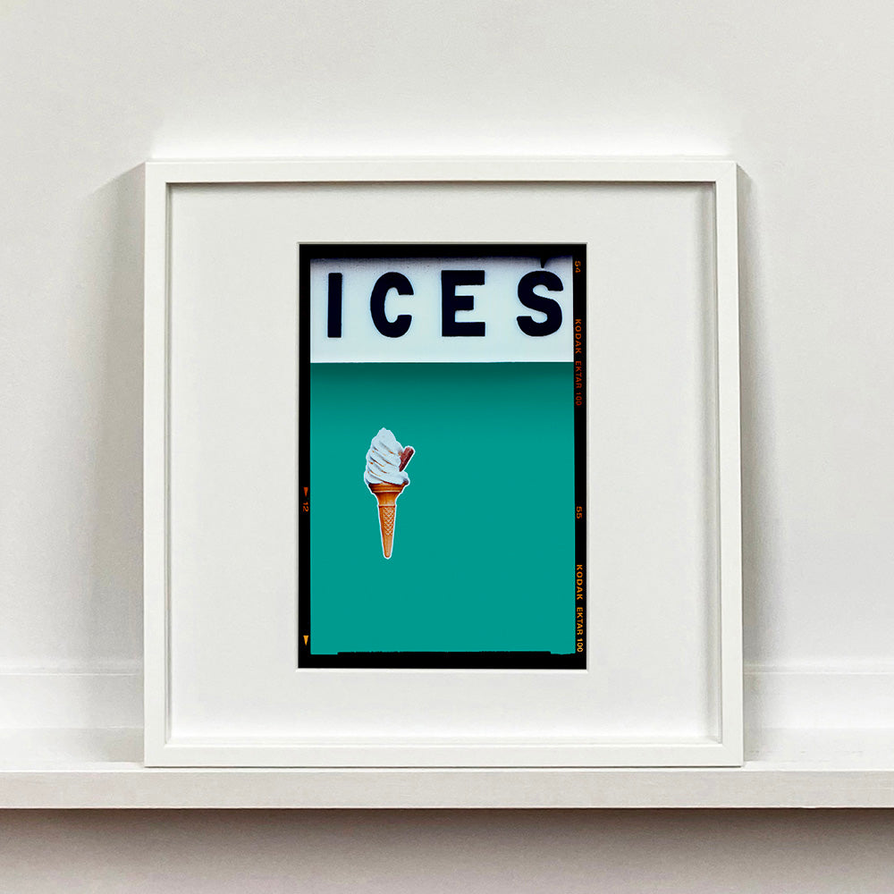 White framed photograph by Richard Heeps.  At the top black letters spell out ICES and below is depicted a 99 icecream cone sitting left of centre against a Turquoise Teal coloured background.  