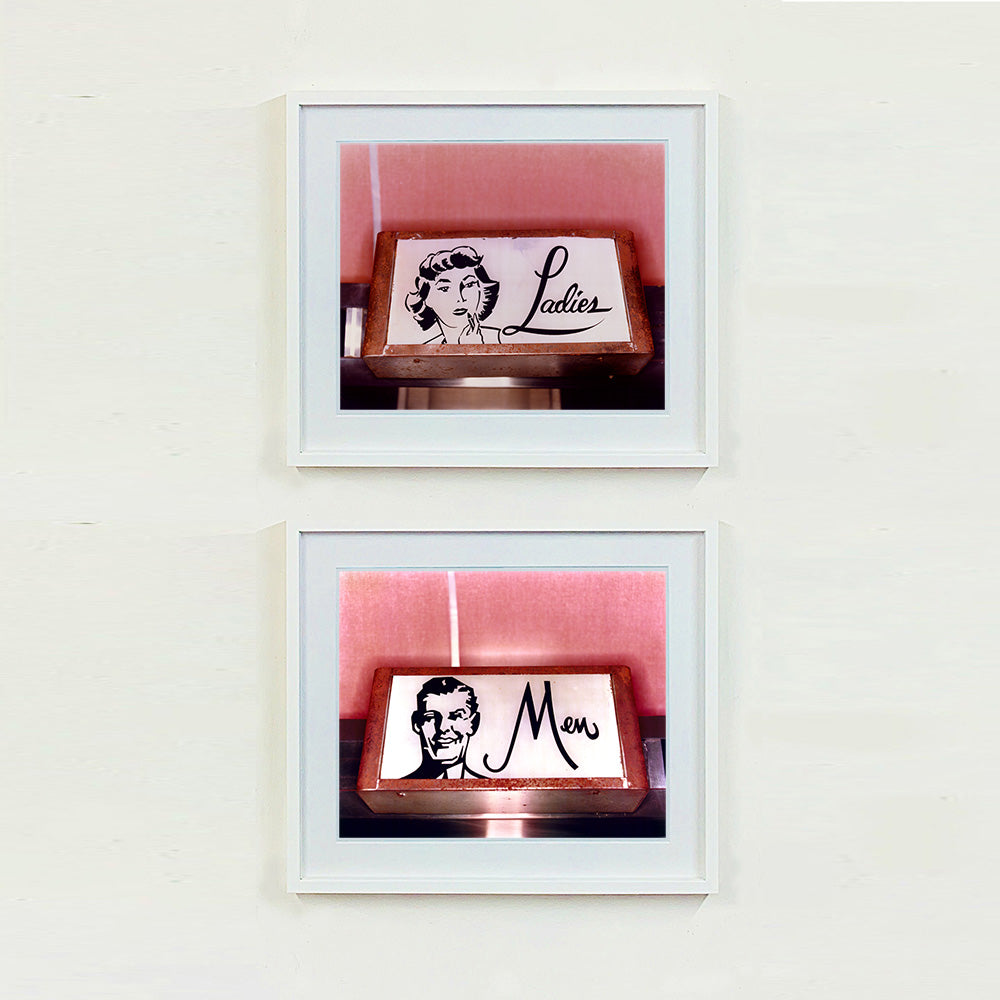 2 white framed photographs by Richard Heeps. Two kitsch toilet signs. Both photographs have a sign one with the word Ladies and one with Men which sits alongside an outline of 1950s woman and man respectively. The signs sit in a wooden frame against a pink tiled wall.