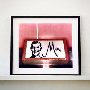 A black framed photograph by Richard Heeps. A kitsch Men's toilet sign. The sign has the word Men alongside an outline of 1950s man. The sign sits in a wooden frame and sits against a pink tiled wall.