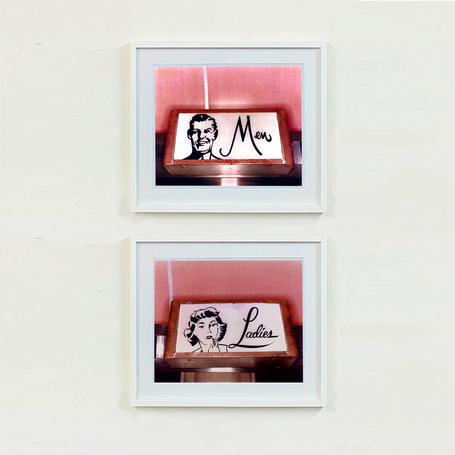 2 white framed photographs by Richard Heeps. Two kitsch toilet signs. Both photographs have a sign one with the word Men and one with Ladies which sits alongside an outline of 1950s man and woman respectively. The signs sit in a wooden frame against a pink tiled wall.