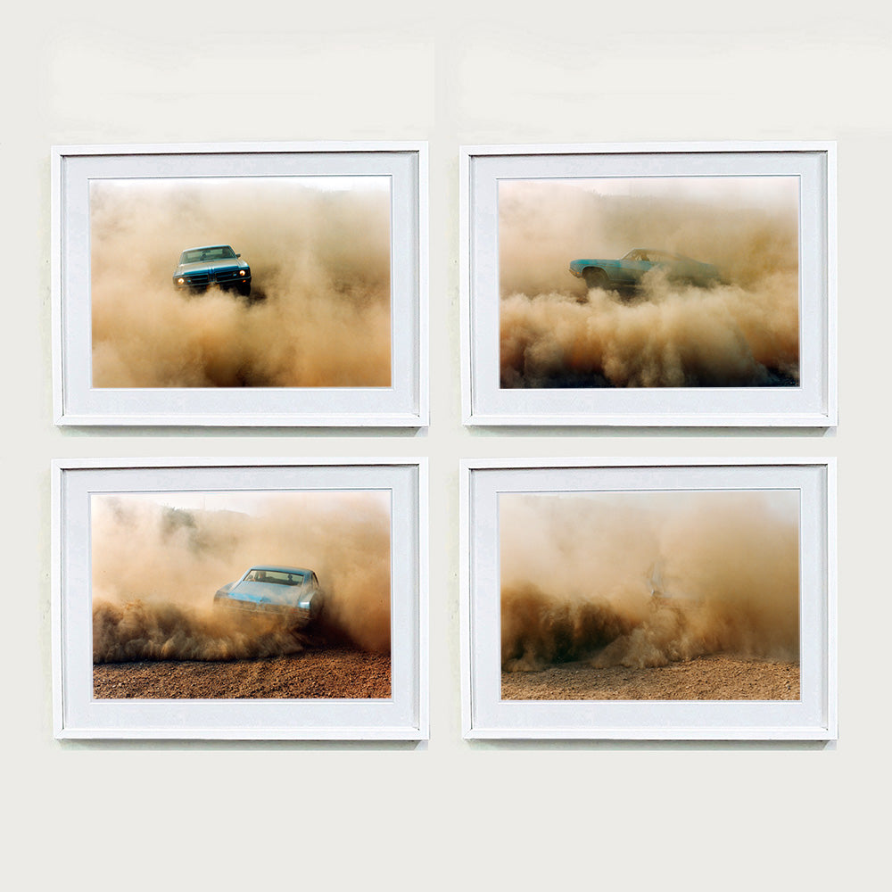 Four white framed photographs by Richard Heeps. The four photographs are of a light blue Buick car moving and slightly obscured by the dust clouds which it has created. The car is sideways on in the first photograph, sideways in the second photograph, head on in the third and can hardly be seen in the fourth photograph.