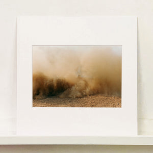 Mounted photograph by Richard Heeps. A vague outline of the back of a light blue Buick car moving and obscured by the dust clouds which it has created.