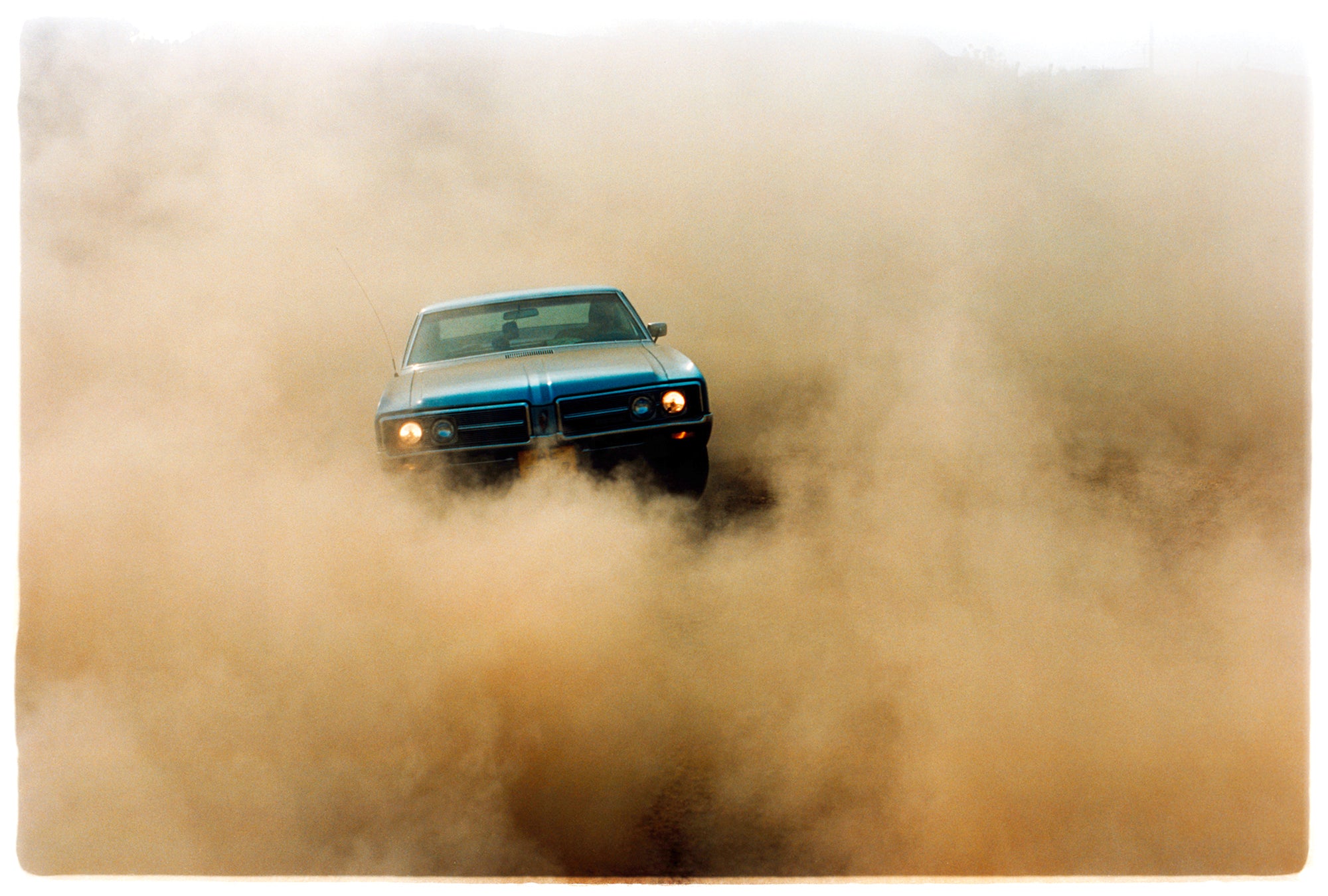 Photograph by Richard Heeps.  A light blue Buick car moving towards the camera and slightly obscured by the dust clouds which it has created.