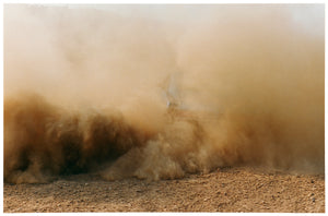 Photograph by Richard Heeps. A vague outline of the back of a light blue Buick car moving and obscured by the dust clouds which it has created.