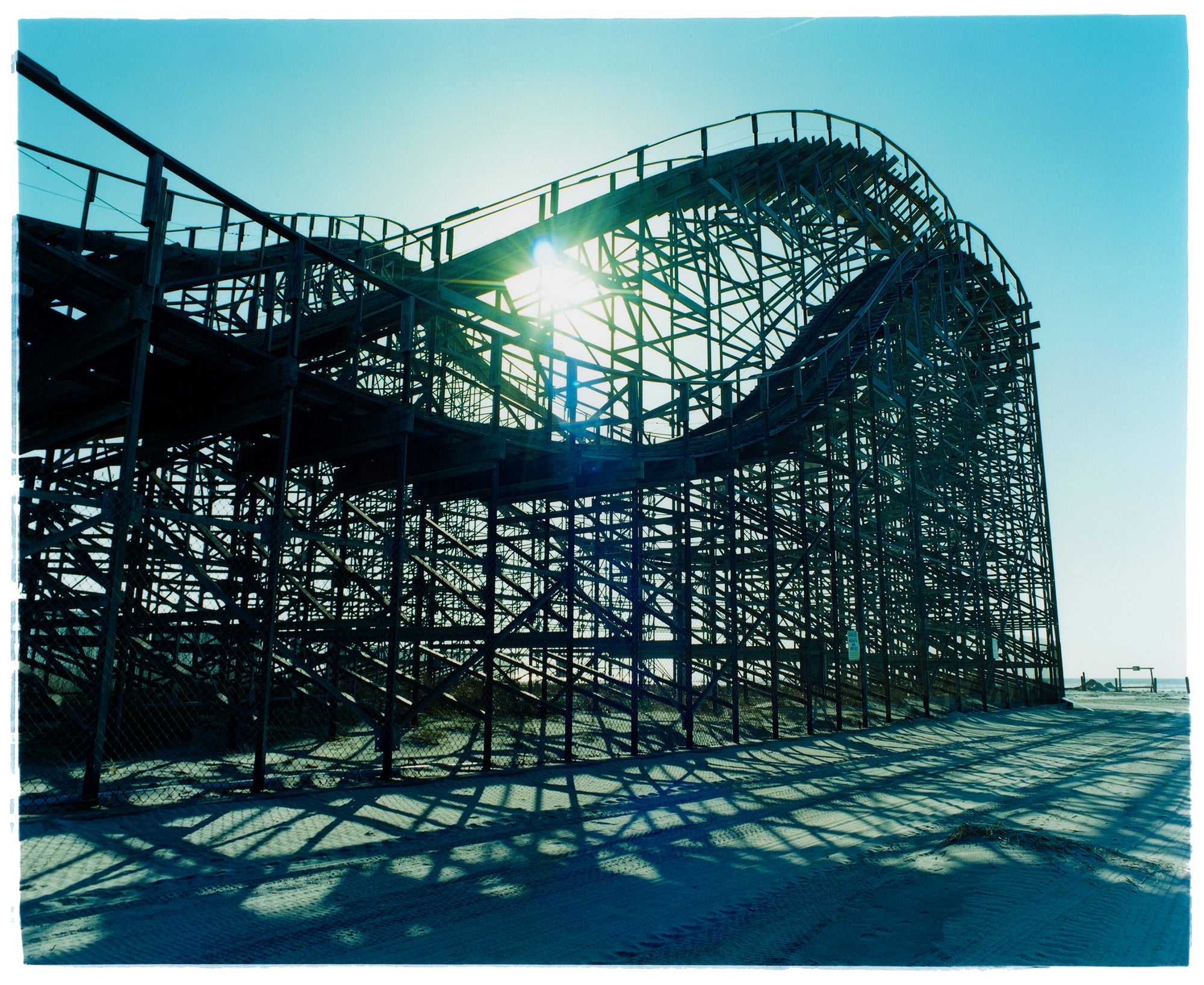 Photograph by Richard Heeps. Great White Roller coaster sits empty on the beach in the setting sun.
