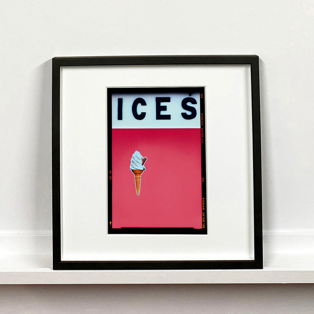 Black framed photograph by Richard Heeps.  At the top black letters spell out ICES and below is depicted a 99 icecream cone sitting left of centre against a coral coloured background.  