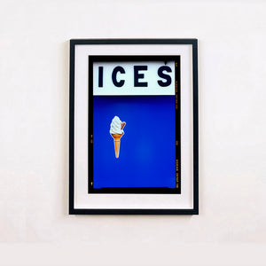 Black framed photograph by Richard Heeps.  At the top black letters spell out ICES and below is depicted a 99 icecream cone sitting left of centre against a blue coloured background.  