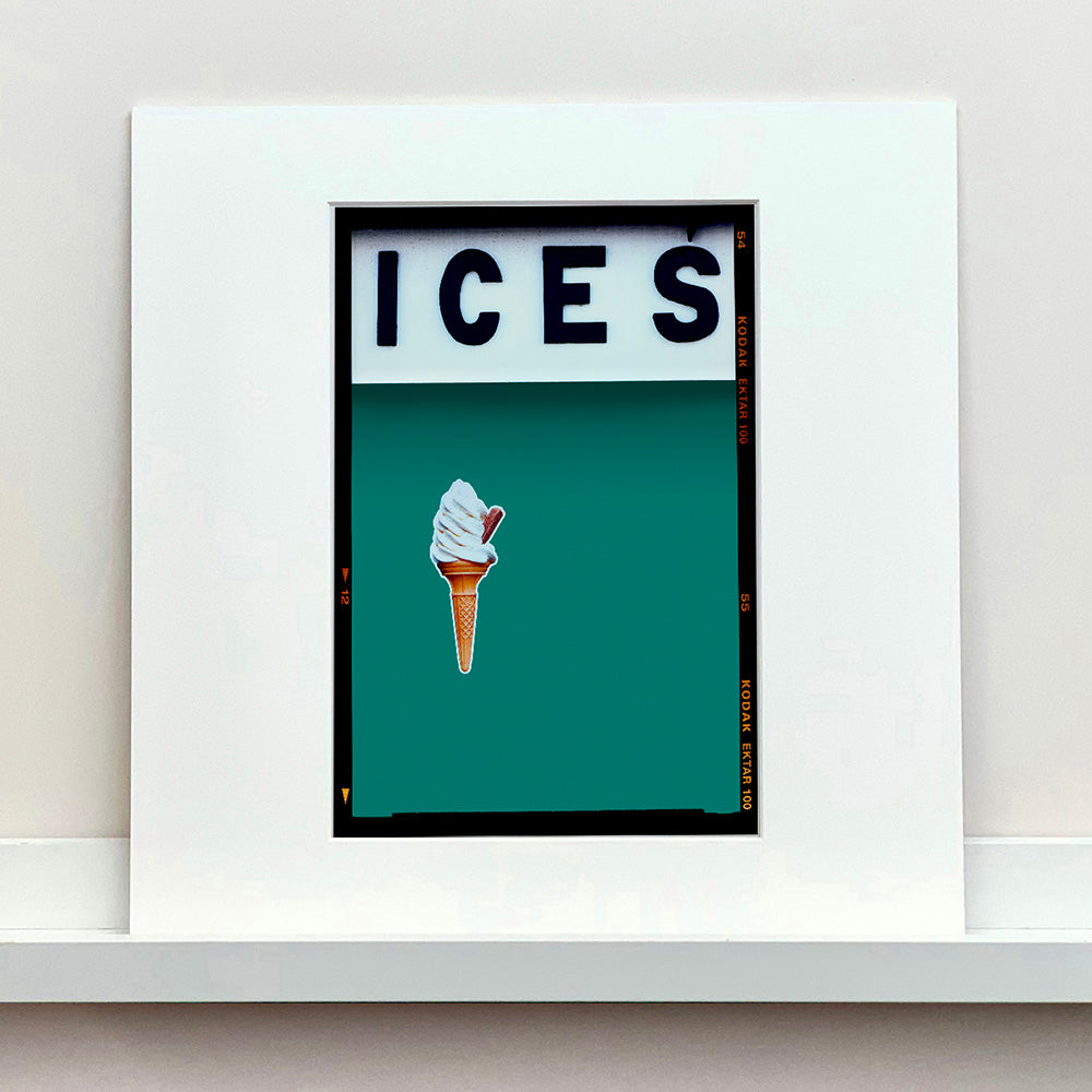 Mounted photograph by Richard Heeps.  At the top black letters spell out ICES and below is depicted a 99 icecream cone sitting left of centre against a deep green teal coloured background.  