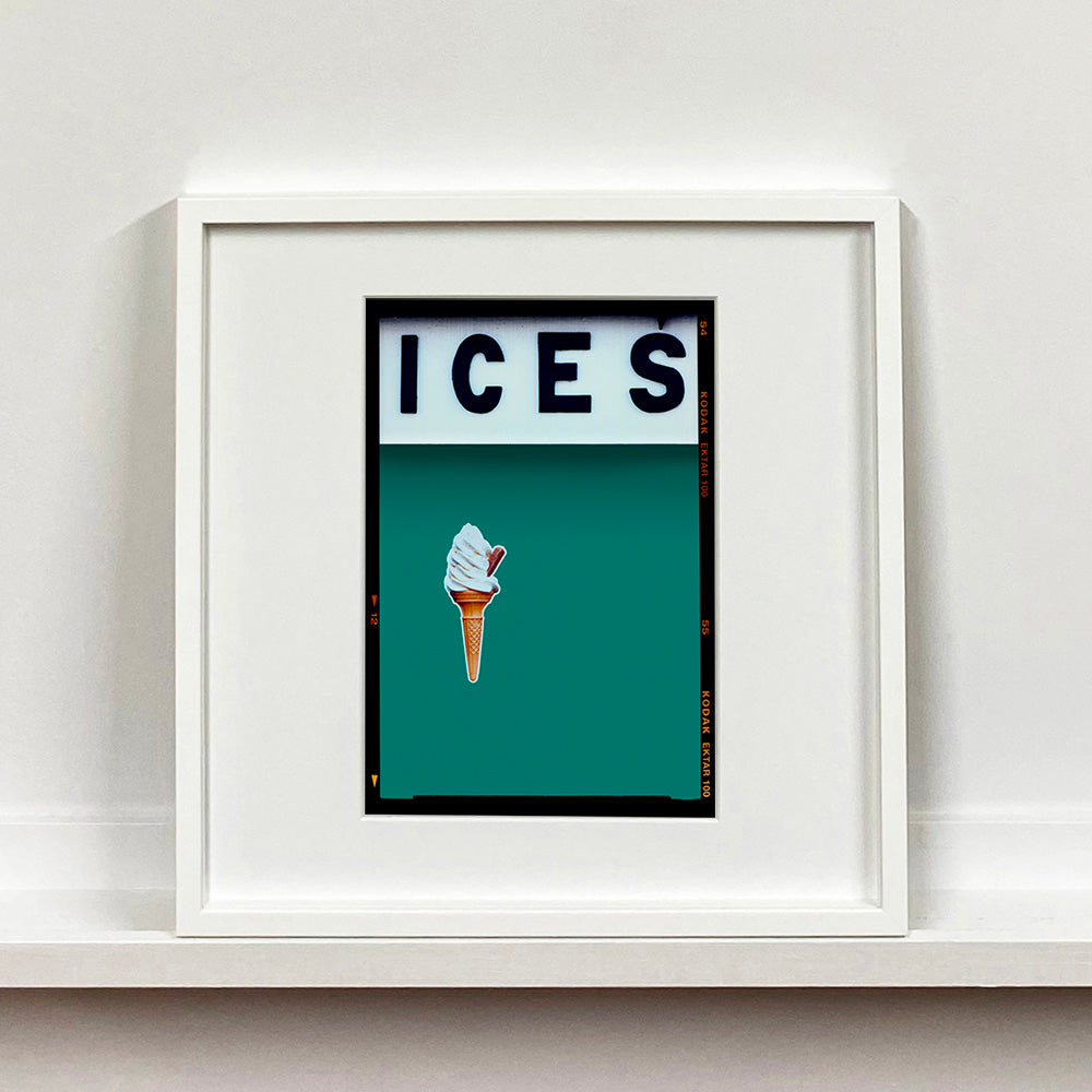 White framed photograph by Richard Heeps.  At the top black letters spell out ICES and below is depicted a 99 icecream cone sitting left of centre against a deep green teal coloured background.  