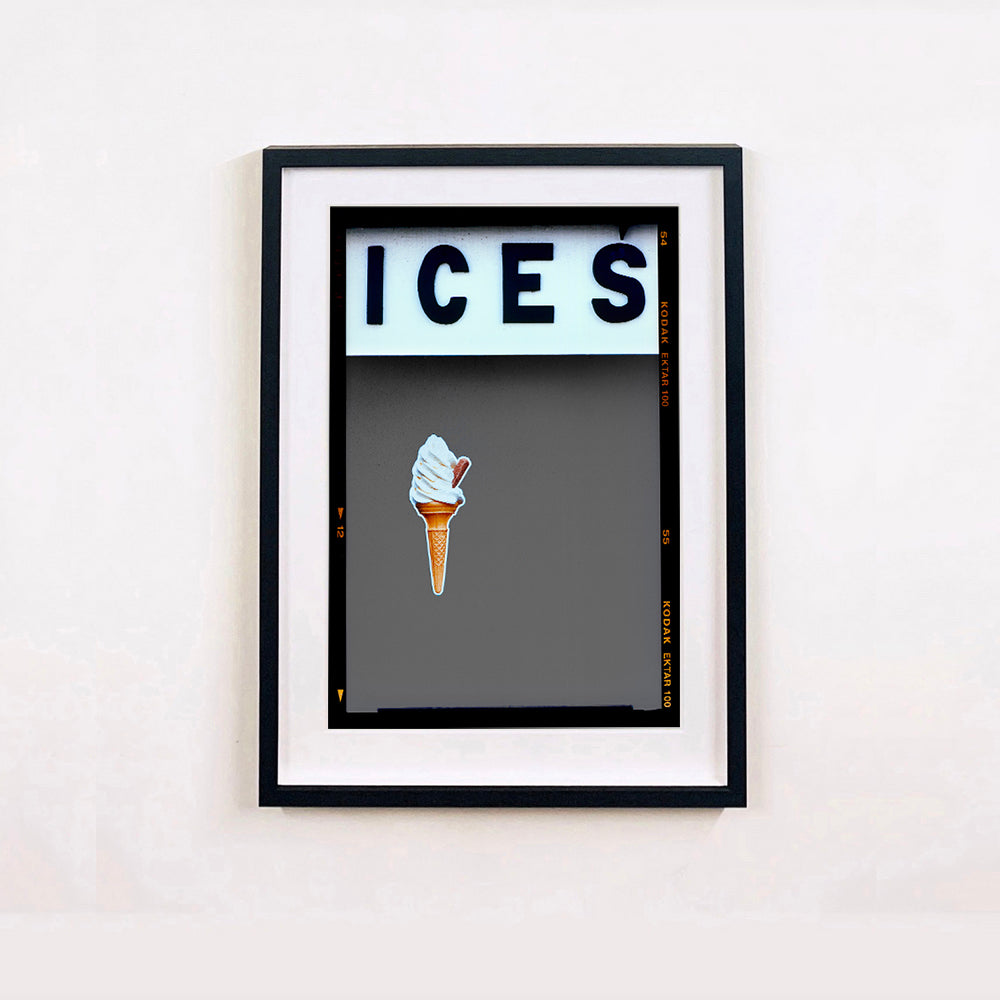 Black framed photograph by Richard Heeps.  At the top black letters spell out ICES and below is depicted a 99 icecream cone sitting left of centre against a grey coloured background.  