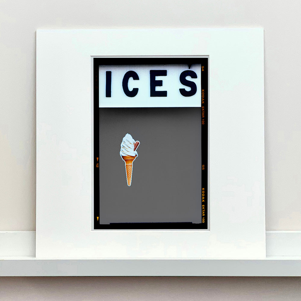 Mounted photograph by Richard Heeps.  At the top black letters spell out ICES and below is depicted a 99 icecream cone sitting left of centre against a grey coloured background.  