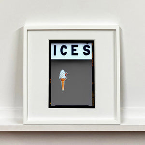White framed photograph by Richard Heeps.  At the top black letters spell out ICES and below is depicted a 99 icecream cone sitting left of centre against a grey coloured background.  