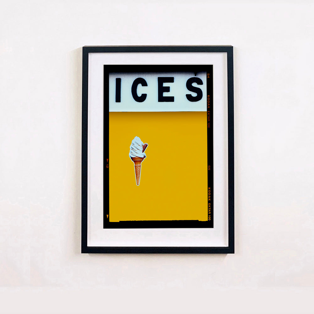 Black framed photograph by Richard Heeps.  At the top black letters spell out ICES and below is depicted a 99 icecream cone sitting left of centre against a mustard yellow coloured background.  