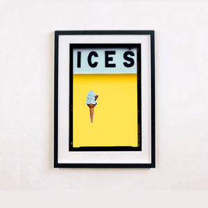 Black framed photograph by Richard Heeps.  At the top black letters spell out ICES and below is depicted a 99 icecream cone sitting left of centre against a sherbert yellow coloured background.  