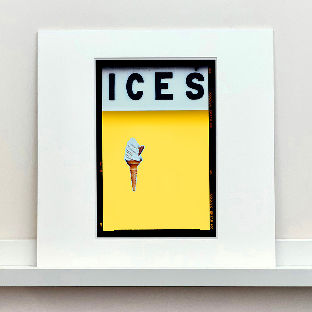 Mounted photograph by Richard Heeps.  At the top black letters spell out ICES and below is depicted a 99 icecream cone sitting left of centre against a sherbet yellow coloured background.  